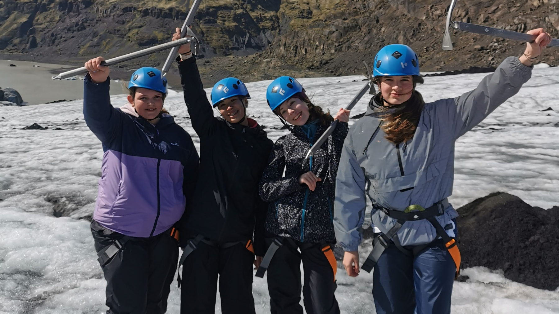 Picture of students standing on a glacier in Iceland holding ice picks in the air